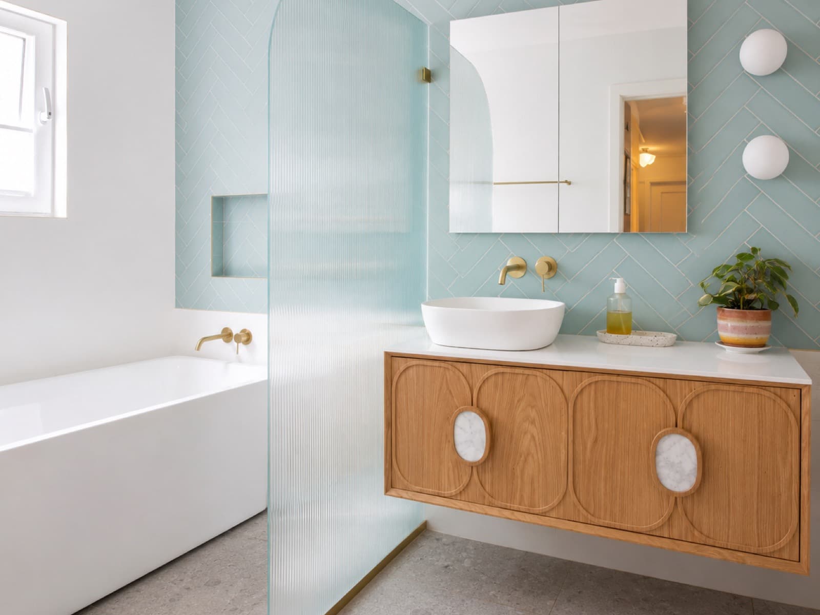 A renovated bathroom in the Tocumwal Revival house, with pale blue herringbone tiling, a fluted glass screen and an oak vanity.